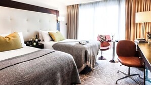 Habitación de hotel con dos camas, un escritorio, una silla y un ventanal con cortinas.