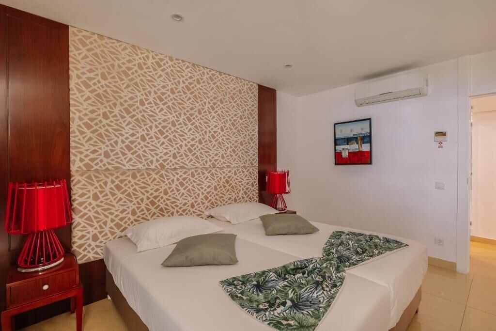 Une chambre d’hôtel avec un lit, deux lampes rouges, un mur à motifs et un tableau encadré accroché au mur.