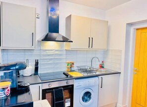 A compact kitchen with a washing machine, a coffee machine, and a sink. - Elegant 1bed flat, sleeps 3, Pet Friendly, Free parking, contractors welcome (Pudsey)