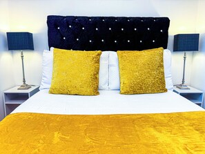 A bed with a white headboard, two yellow pillows, and a yellow bedspread. There are two bedside lamps on either side of the bed.