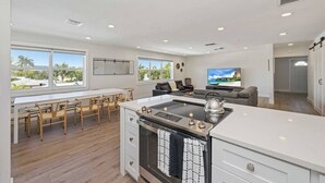 Een moderne keuken met een centraal eiland, een eethoek met houten stoelen en een woongedeelte met een bank en televisie.