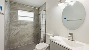 Een badkamer met douche, toilet, wastafel en spiegel.