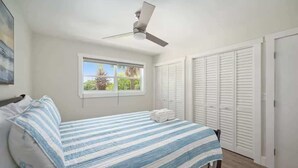 Een slaapkamer met een bed, een plafondventilator, een raam en witte kasten.