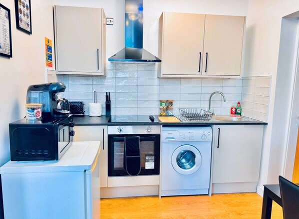 A compact kitchen with a microwave, oven, and washing machine, white cabinets, and a tiled backsplash.