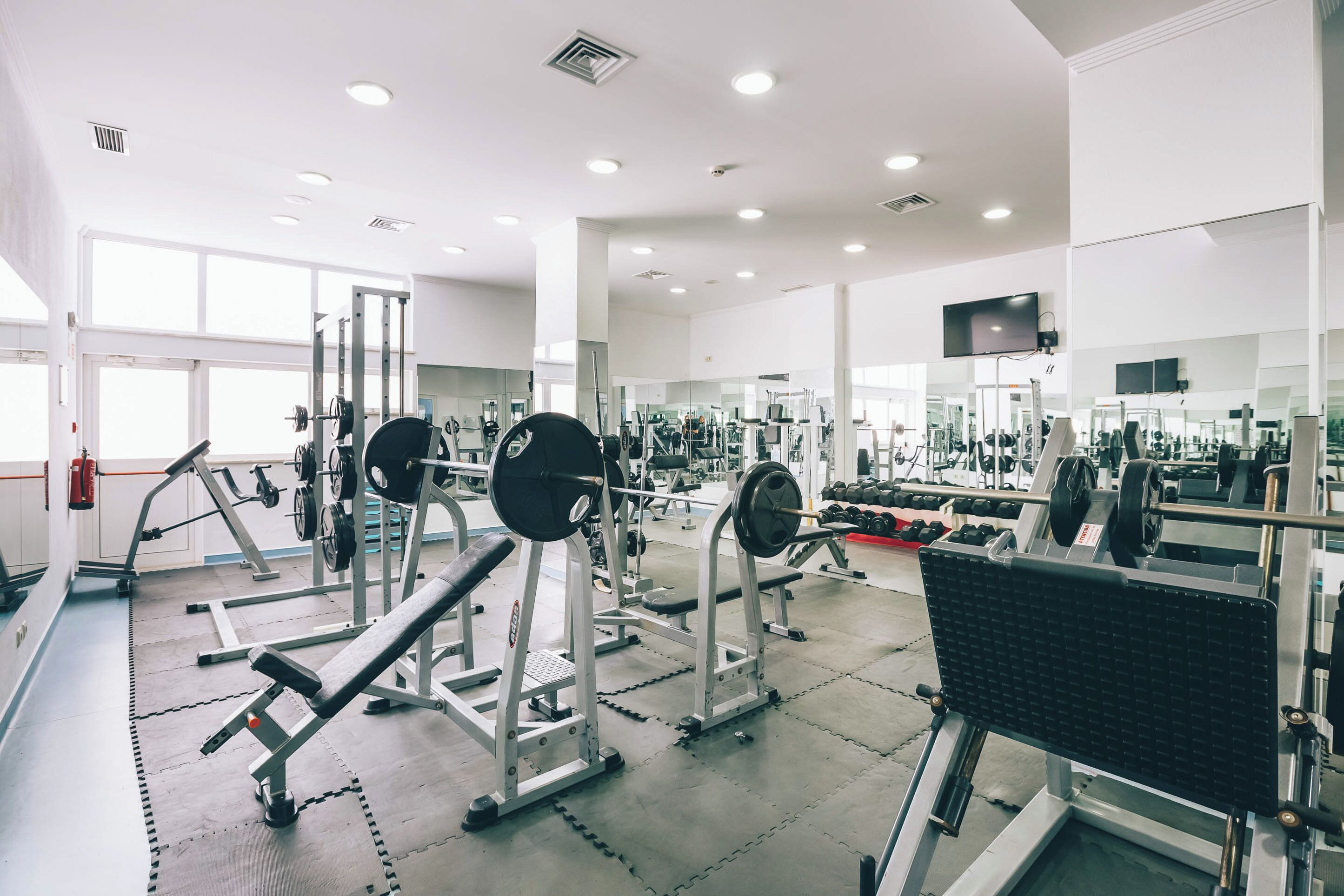 Ein Fitnessstudio mit Gewichten, Spiegeln und einem Fernseher.