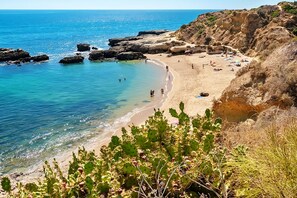 A beach with clear blue water, rocky cliffs, and people enjoying the sun. - An Undeniable Jewel in Albufeira! Indoor and Outdoor Pools, Spa, Free Parking! (Albufeira)