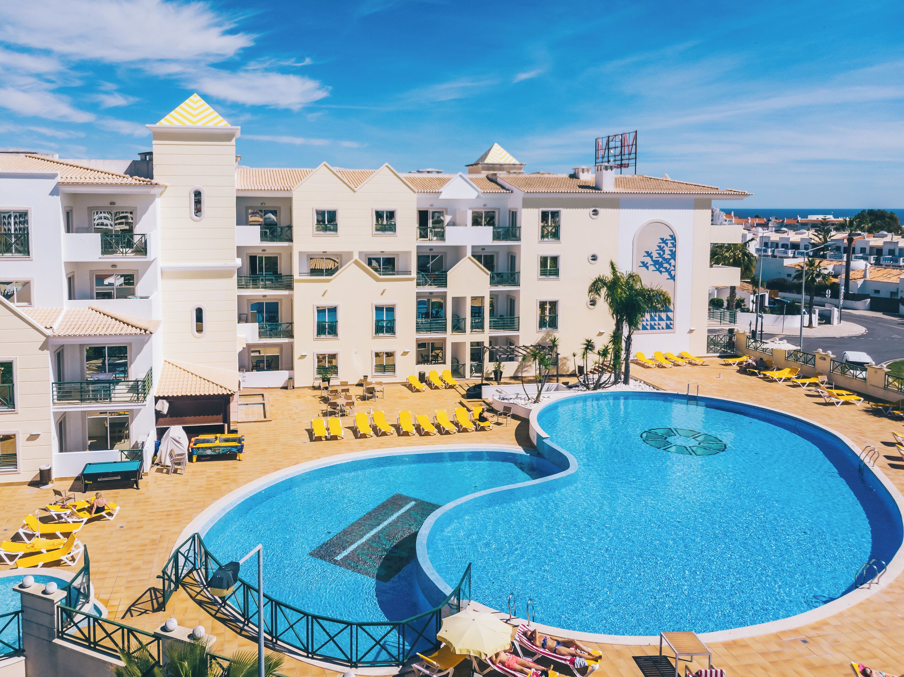 A resort with a large pool, multiple balconies, and a view of the sea.