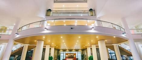 Een meerlaags atrium met een centraal open gedeelte, glazen balustrades en een trap.