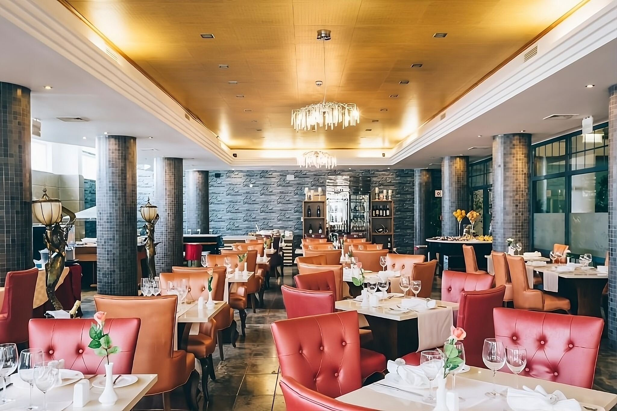 A restaurant with red upholstered chairs, white tablecloths, and a chandelier.