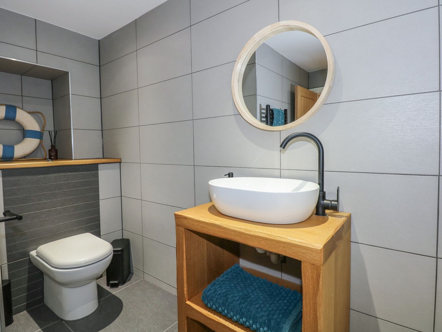 A modern bathroom with a white toilet, a wooden vanity with a sink, and a round mirror above the sink.