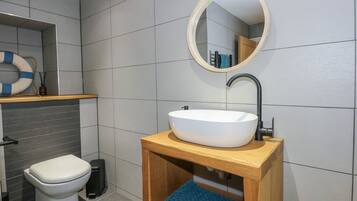 A modern bathroom with a white toilet, a wooden vanity with a sink, and a round mirror above the sink.
