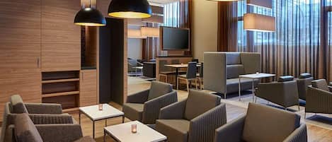 A modern hotel lobby with seating areas, a TV, and large windows.