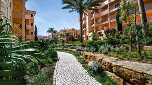 A pathway lined with greenery and palm trees, leading to a building with balconies. - Boat Tour from Praia da Luz! Full Kitchen, Indoor and Outdoor Swimming Pools! (Luz)