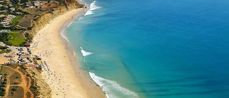 An aerial view of a coastal area with a sandy beach, clear blue waters, and a rugged coastline.