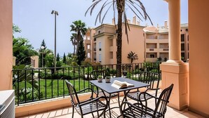 A balcony with a table and chairs, overlooking a well-maintained garden and a building with multiple balconies. - Best Place to Unwind! Free Parking, Full Kitchen, Outdoor and Indoor Pools! (Luz)