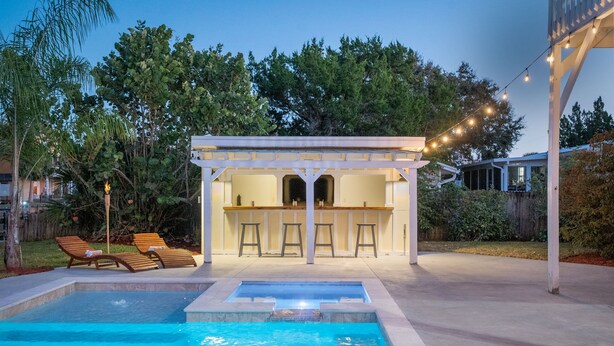 Area piscina con lettini, un bar e un pergolato con luci a catena.