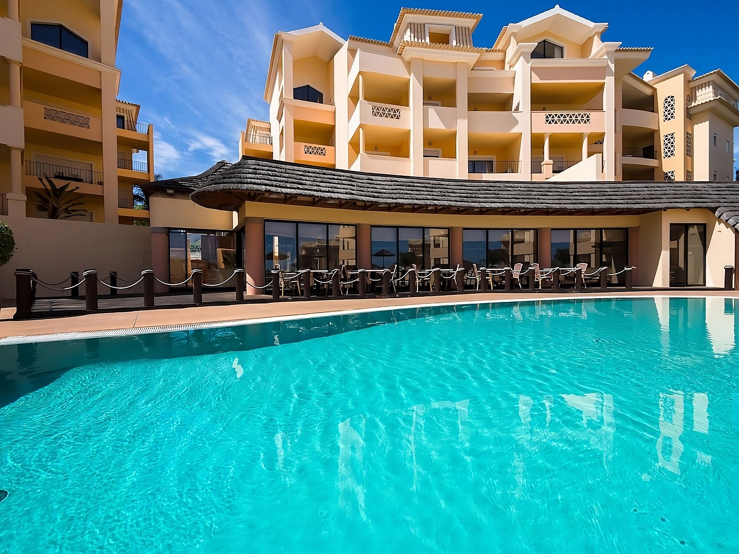 Et hotel med swimmingpool, flere balkoner og et overdækket siddeområde.
