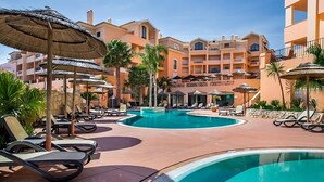 A resort pool area with lounge chairs, umbrellas, and a building with balconies.