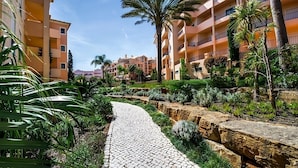 A pathway lined with greenery and palm trees, leading to a building with balconies. - Your Home Away From Home! Fully-equipped Kitchen, 3 Swimming Pool, Free Parking! (Luz)