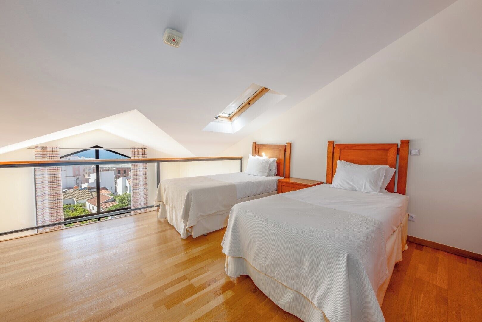 Una camera da letto con due letti, un lucernario e un balcone con vista sugli edifici.