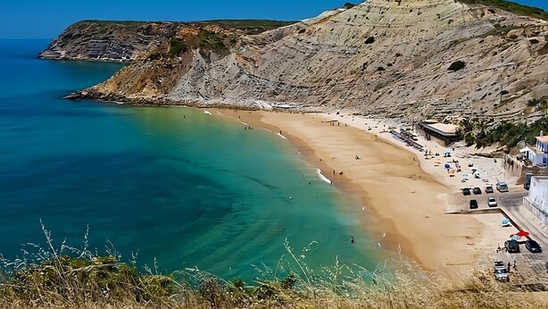 A coastal beach with clear turquoise waters, a sandy shore, and rocky cliffs.