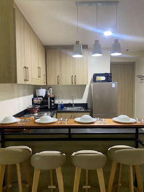 A modern kitchen with wooden cabinets, a microwave, a stove, and a sink. There are four stools and a dining table set for four.