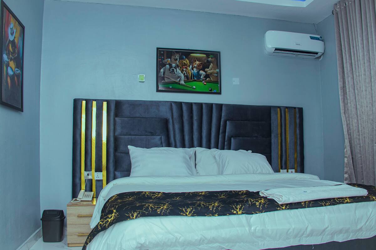 Cama bem arrumada com cabeceira escura, um quadro na parede e um aparelho de ar condicionado.