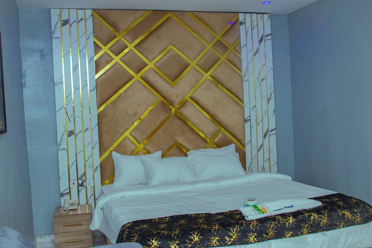 Quarto de hotel com uma cama, uma mesinha de cabeceira de madeira e uma parede com padrão geométrico.