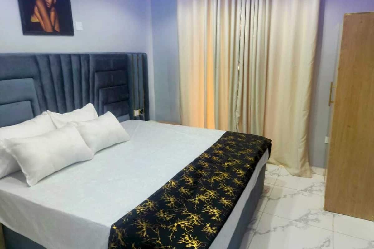 Cama bem arrumada com lençóis brancos e uma colcha preta com padrão amarelo.