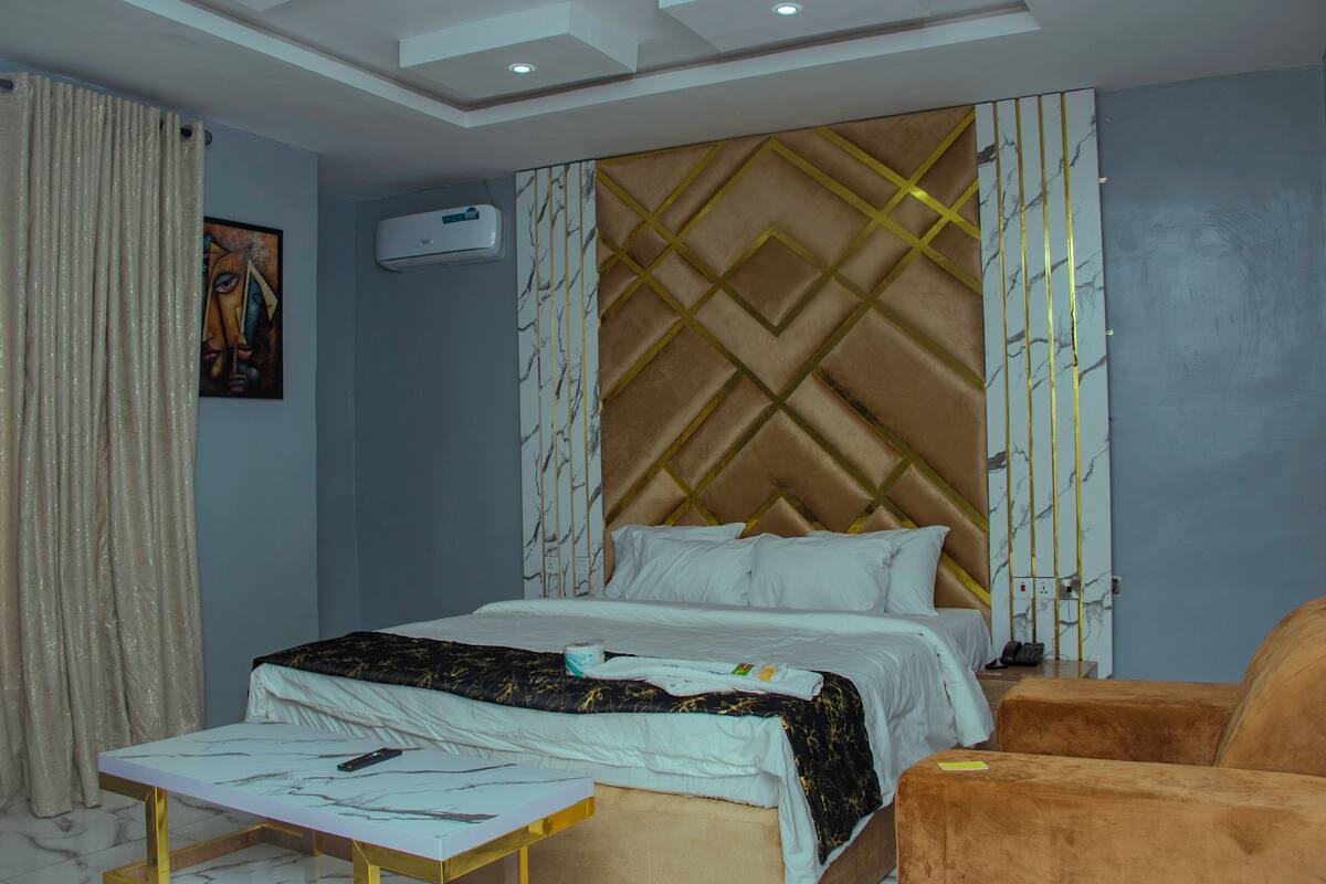 Quarto de hotel com cama, mesa de cabeceira, cadeira e ar-condicionado fixado na parede.