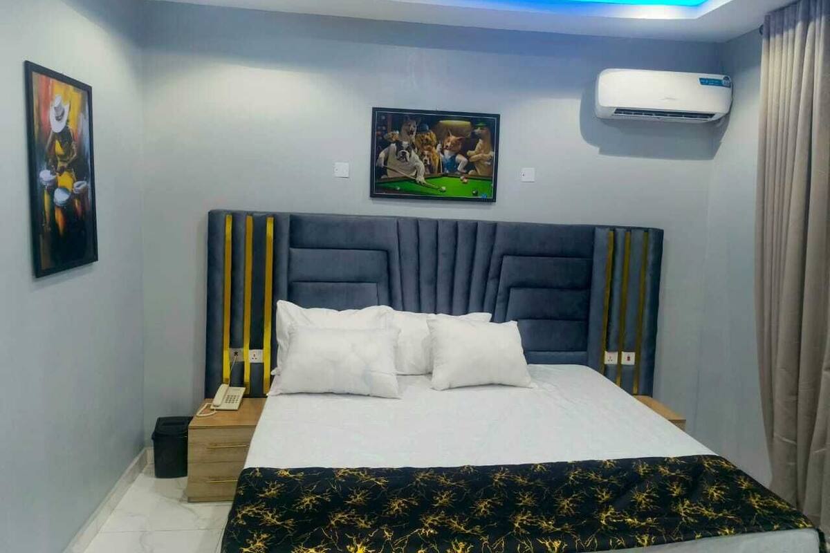 Quarto moderno com uma cama grande, cabeceira com listras verticais, ar condicionado fixado na parede e um quadro com pessoas jogando bilhar.