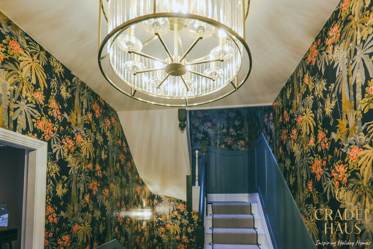 A staircase with floral wallpaper, a chandelier, and a staircase railing.