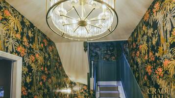 A staircase with floral wallpaper, a chandelier, and a staircase railing.