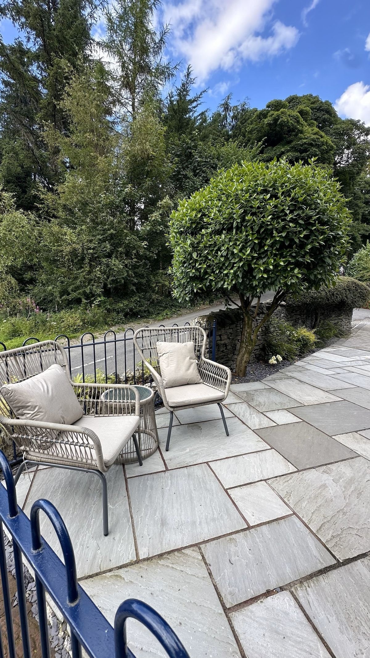A patio with two wicker chairs and a stone wall.