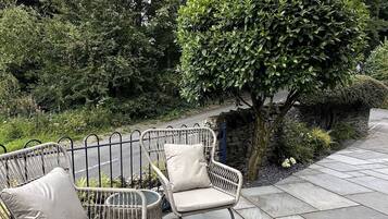 A patio with two wicker chairs and a stone wall.