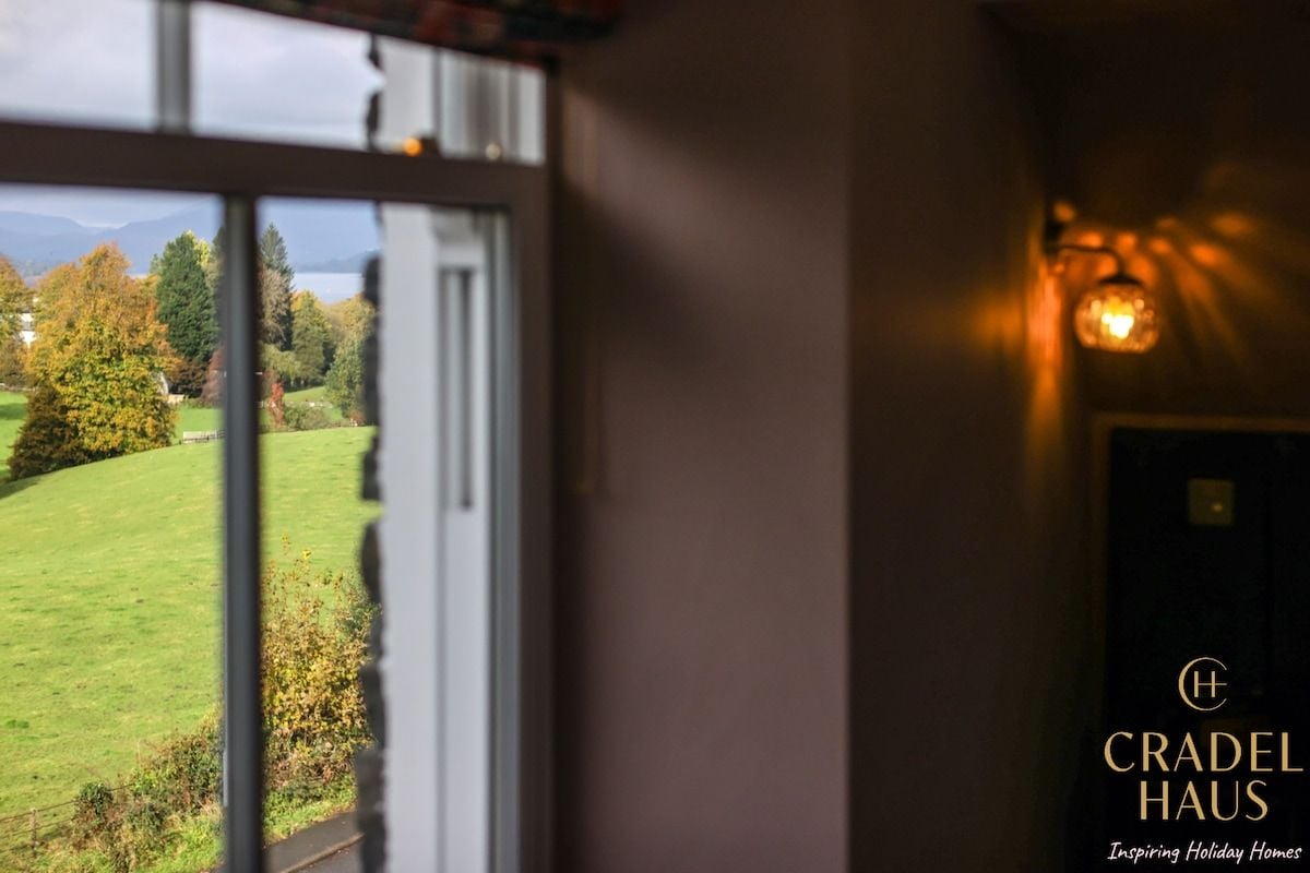 A view through a window with a landscape outside, a door with a logo, and a wall-mounted light fixture.