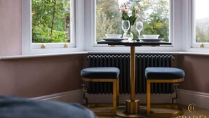 Een zithoek met eettafel voor twee personen, twee krukken en uitzicht op groen buiten het raam.
