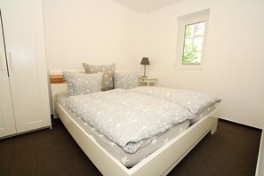Une chambre à coucher comprenant un lit, une table de chevet, une lampe, une fenêtre et une armoire.