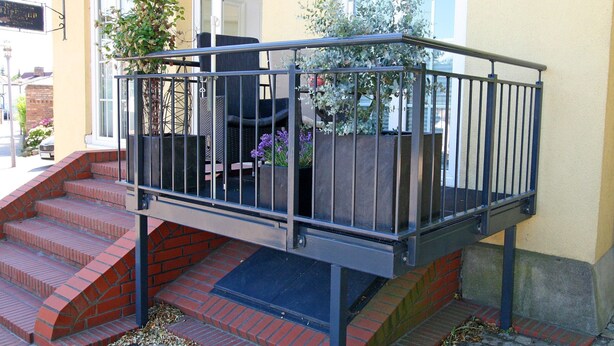 A staircase leading to a balcony with a metal railing, potted plants, and a building entrance. - Modernes Appartement mit Balkon, Wiek (Wiek)