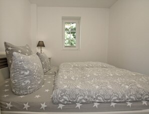 A bedroom with a bed, pillows, a nightstand, a lamp, and a window.