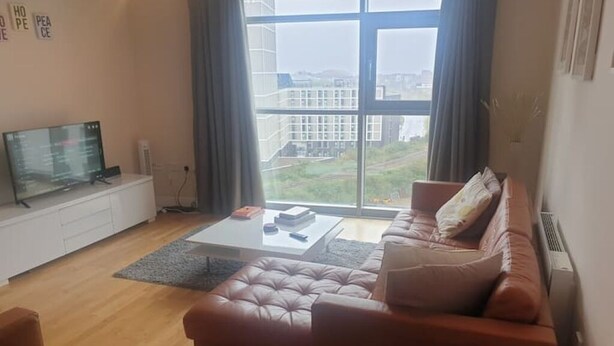 A modern living room with a leather sofa, a coffee table, and a TV on a white cabinet. - Modern City-Centre Apartment with Stunning Views & Free Parking (Cardiff)