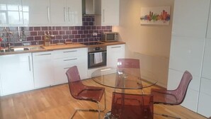 A modern kitchen with white cabinets, a microwave, and a glass dining table with chairs. - Modern City-Centre Apartment with Stunning Views & Free Parking (Cardiff)