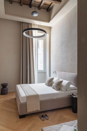 Une chambre moderne avec un grand lit, un luminaire suspendu, une fenêtre avec des rideaux et un plancher en bois.