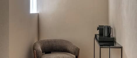 Una habitación pequeña y moderna con un sofá marrón, una mesita y un soporte metálico con una tetera.