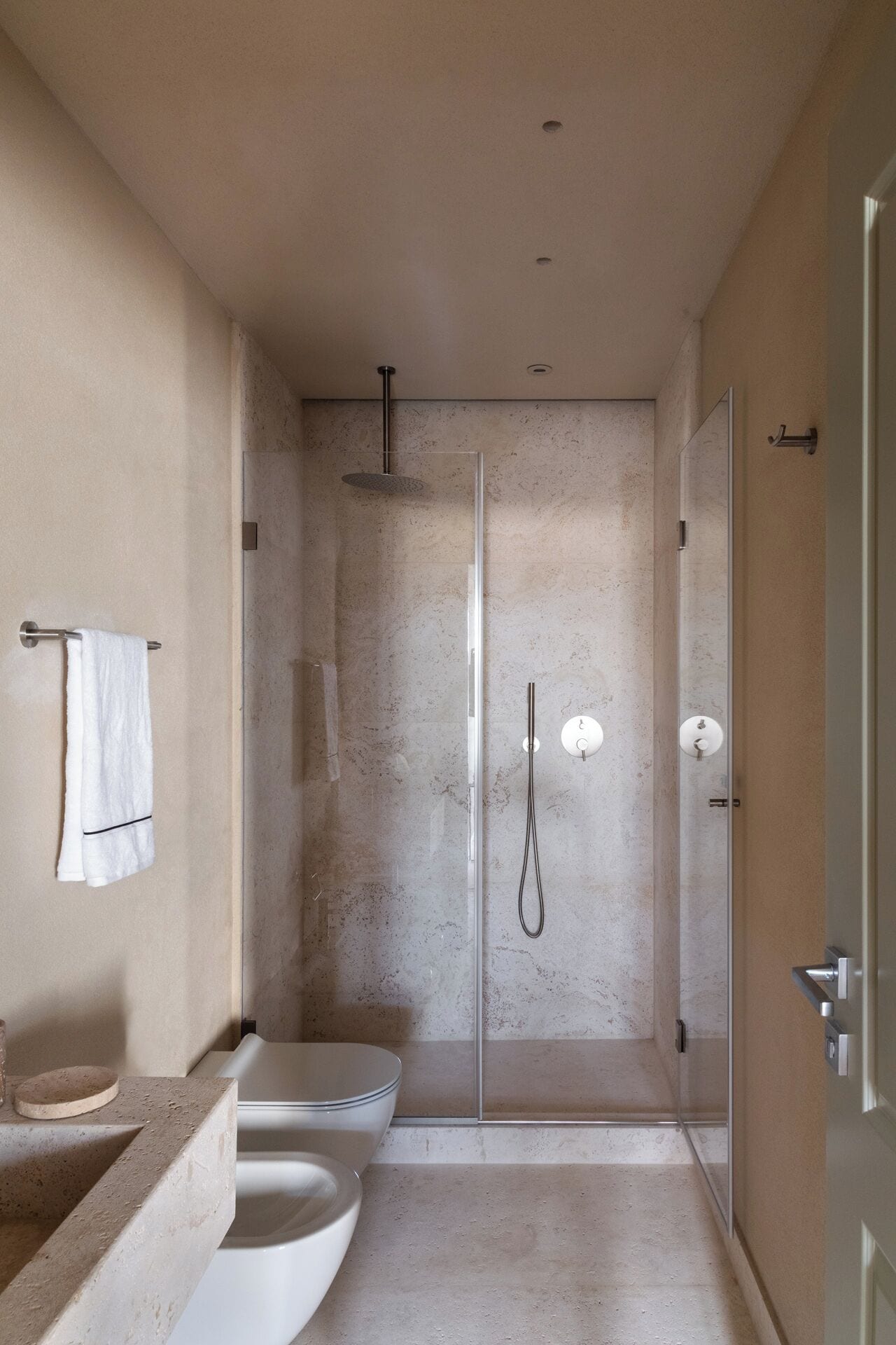A modern bathroom with a glass-enclosed shower, a toilet, and a sink with a marble countertop.