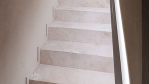 Un escalier avec des marches blanches et une rampe blanche, menant à un palier où se trouve un luminaire.