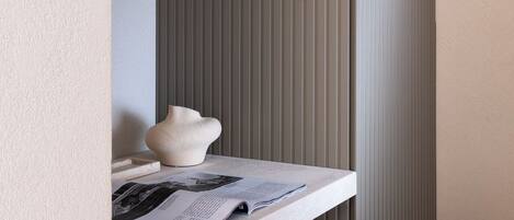 A modern room with a built-in shelf holding a vase and a magazine, a textured chair, and a vertical striped wall.