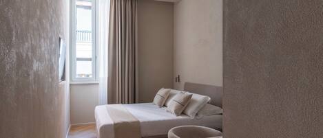 A bedroom with a bed, a chair, a window with curtains, and a door.