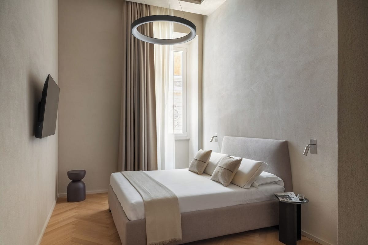 Une chambre moderne avec un grand lit, une table de chevet, un téléviseur fixé au mur et une fenêtre avec des rideaux.