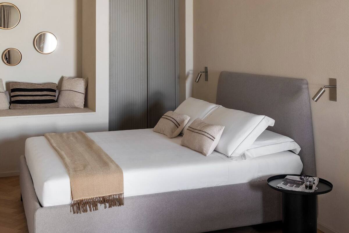 Une chambre moderne avec un lit, une table de chevet et un petit coin salon agrémenté de coussins.